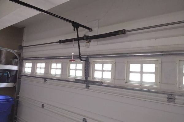 Garage door spring repair in Suffolk VA: the torsion spring pair on the shaft of a North Suffolk door before replacement, opener rail and red emergency release in front