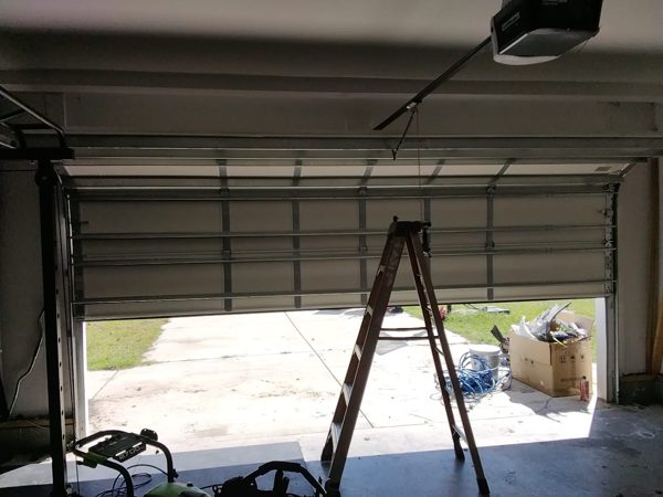 Garage door out of balance fixed in Suffolk VA: the same door after the spring adjustment, sitting at the halfway point with a ladder underneath